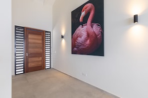 A hallway with a wooden door, a large flamingo painting, and a wall-mounted light fixture. - Villa Dushi Brisa 650 (Sint Willibrordus)
