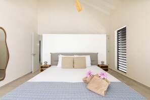 A bedroom with a bed, bedside tables, a mirror, a window with blinds, and a towel with flowers on the bed. - Villa Dushi Brisa 650 (Sint Willibrordus)