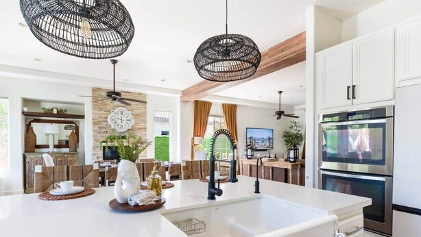 Cozinha moderna com armários brancos, uma ilha grande, eletrodomésticos de aço inoxidável e duas luminárias pendentes pretas.