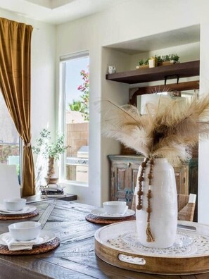 A dining table with a white vase, a window with curtains, and a shelf with decorative items. - Secluded Sanctuary/ Pool/Spa/Casita/BNP/Coachella/Luxury Oasis/Gated Community (La Quinta)