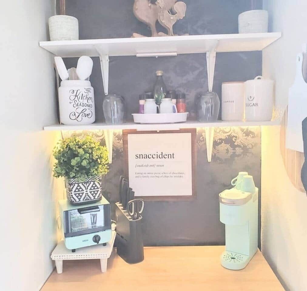 A kitchen area with shelves holding kitchenware, a framed sign, a toaster, and a water dispenser.