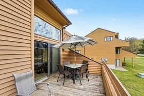 A deck with a table and chairs, a glass door, and a view of neighboring houses. - Spacious 3 bdrm, 2 Bath Plus Loft, 1630 Sq Ft.  Many onsite amenities with Golf/Skiing near by! (Harbor Springs)