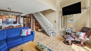 A living room with a blue sofa, a recliner, a wooden coffee table, a staircase, and a kitchen in the background. - Spacious 3 bdrm, 2 Bath Plus Loft, 1630 Sq Ft.  Many onsite amenities with Golf/Skiing near by! (Harbor Springs)