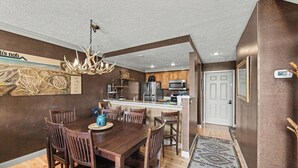 A dining area with a wooden table and chairs, a chandelier, and a kitchen in the background. - Spacious 3 bdrm, 2 Bath Plus Loft, 1630 Sq Ft.  Many onsite amenities with Golf/Skiing near by! (Harbor Springs)
