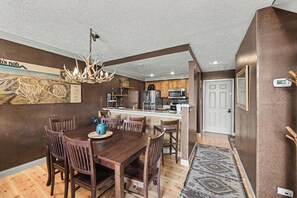 A dining area with a wooden table and chairs, a chandelier, and a kitchen in the background. - Spacious 3 bdrm, 2 Bath Plus Loft, 1630 Sq Ft.  Many onsite amenities with Golf/Skiing near by! (Harbor Springs)