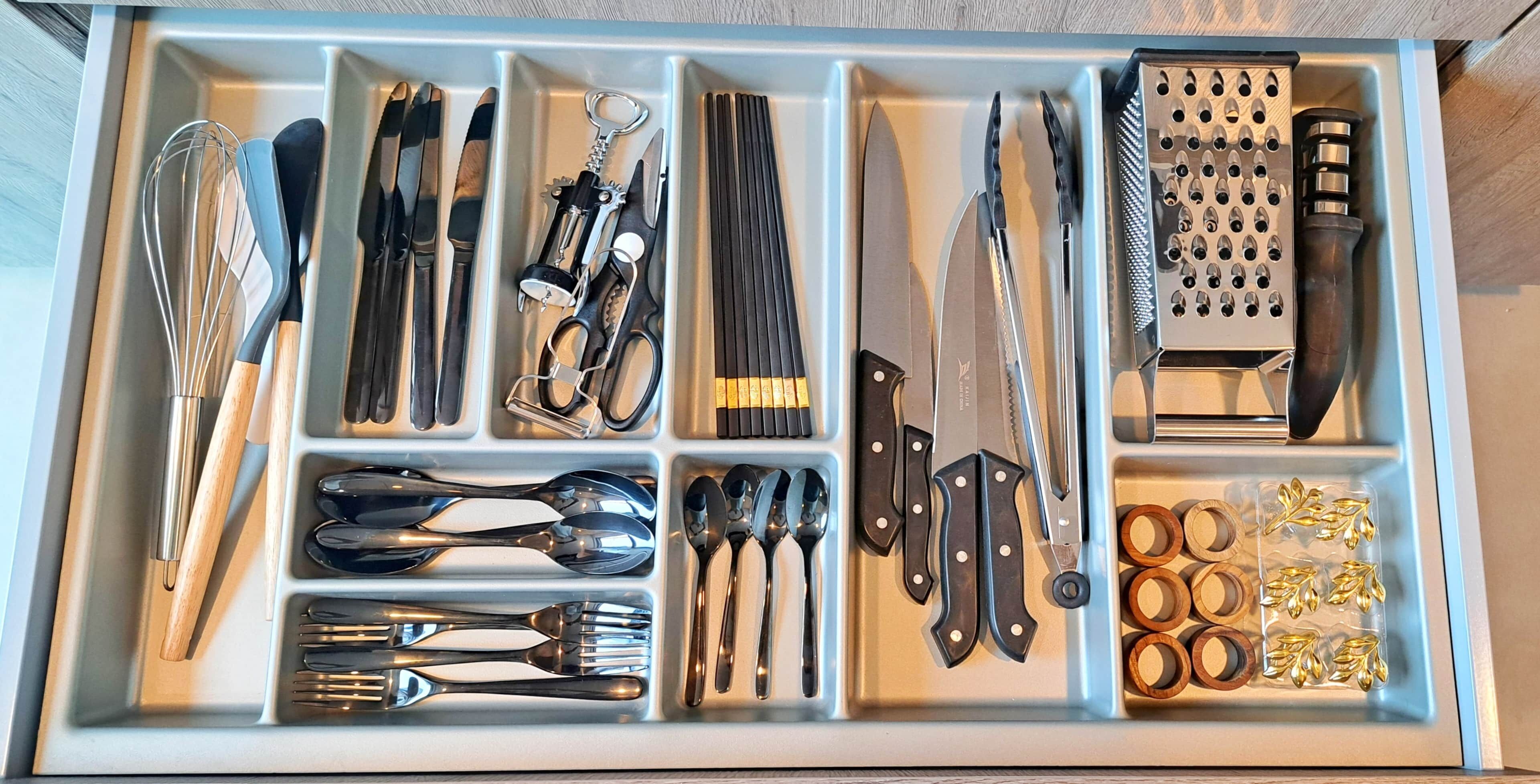 Un tiroir contenant divers ustensiles et outils de cuisine, rangés dans des compartiments.