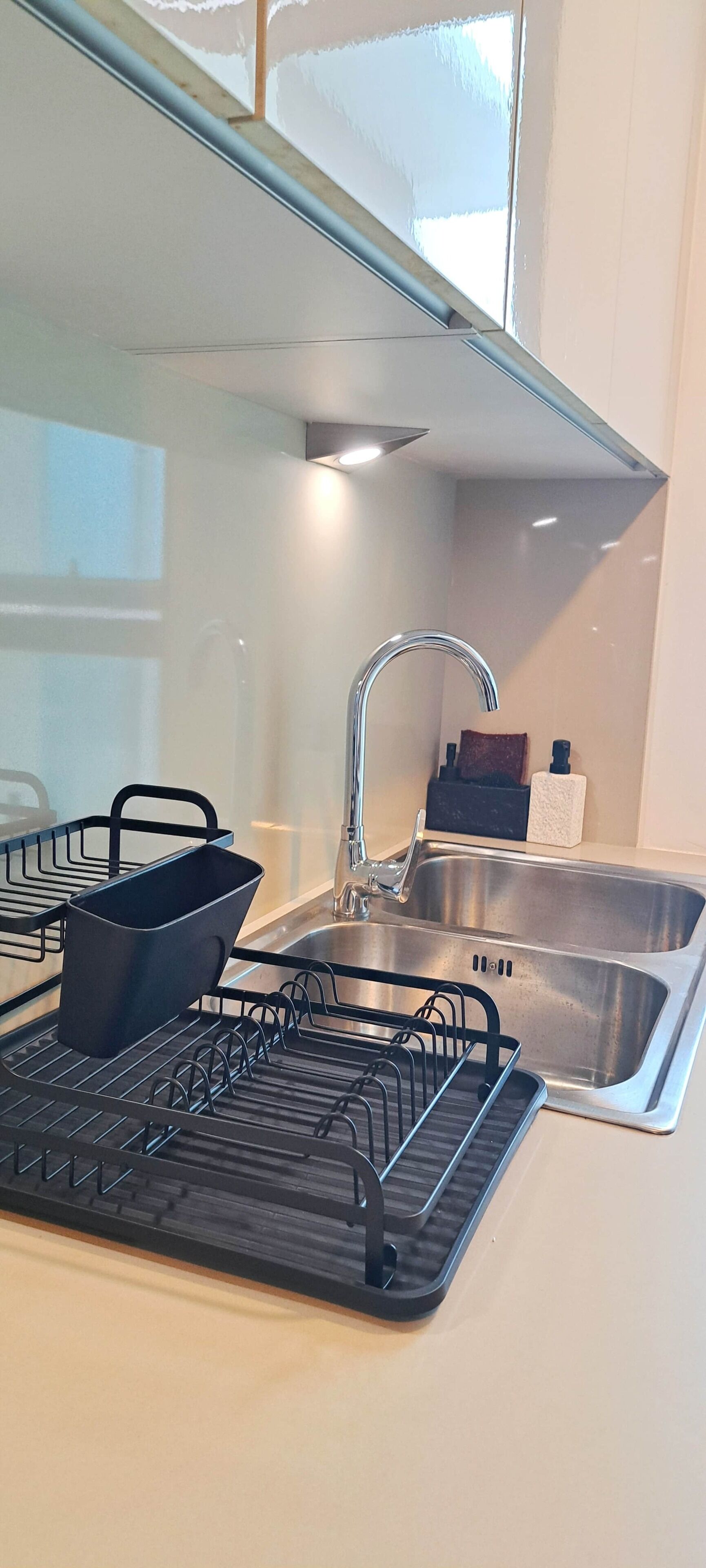 A kitchen with a stainless steel sink, a black dish rack, and a window above the sink.
