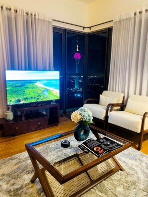 Una sala de estar moderna con un televisor de pantalla plana, una mesa de centro con una revista, un sofá y vistas de un paisaje urbano nocturno.