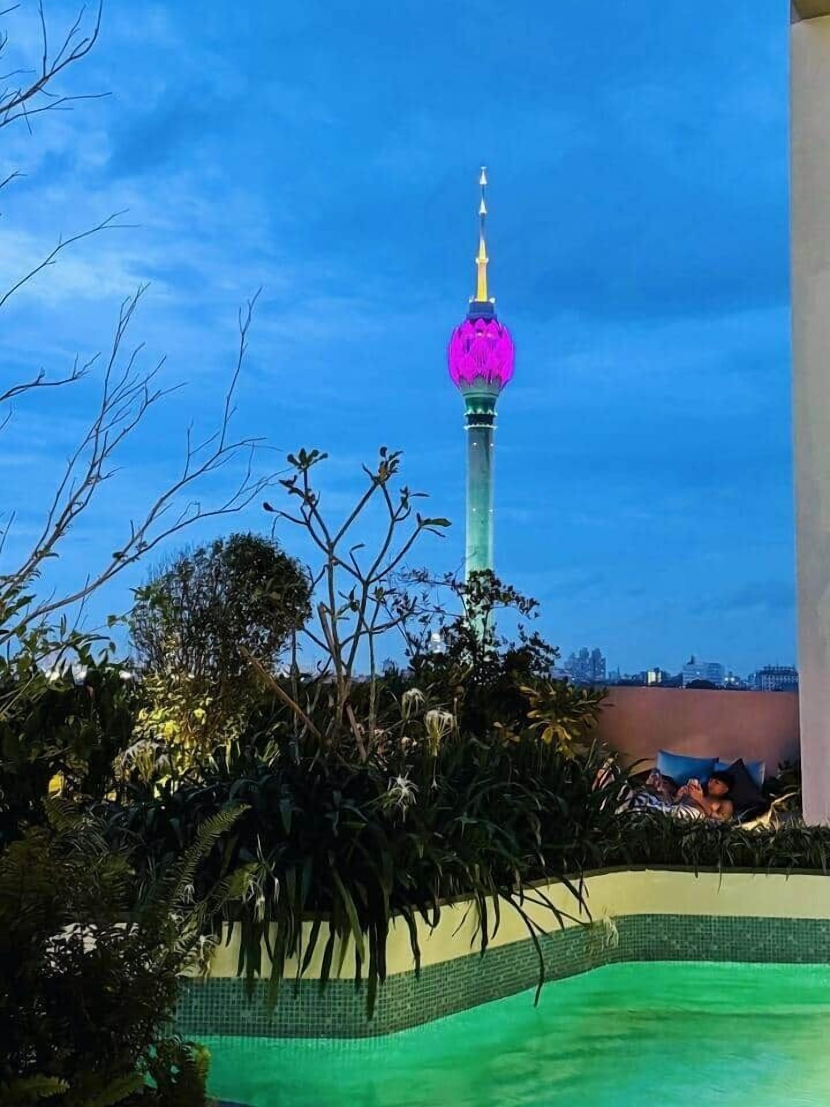 A view of a tower with a spherical top, surrounded by greenery and a pool area.