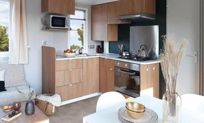 A compact kitchen with wooden cabinets, a microwave, a stove, and a dining area with a table and chairs. - Beach 1km, 4/6 pers, St Georges - ile d'Oléron (Saint-Georges-d'Oléron)