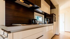 Eine moderne Küche mit dunkler Holzrückwand, weißen Schränken und Edelstahlgeräten.