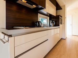 Eine moderne Küche mit dunkler Holzrückwand, weißen Schränken und Edelstahlgeräten.