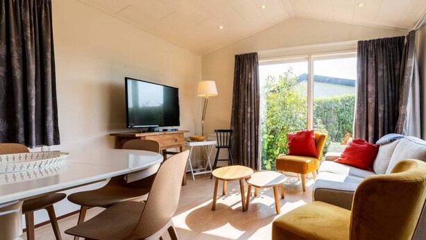 Ein modernes Wohnzimmer mit einem Flachbildfernseher, einem Esstisch, Stühlen, einer Couch und Blick ins Grüne.