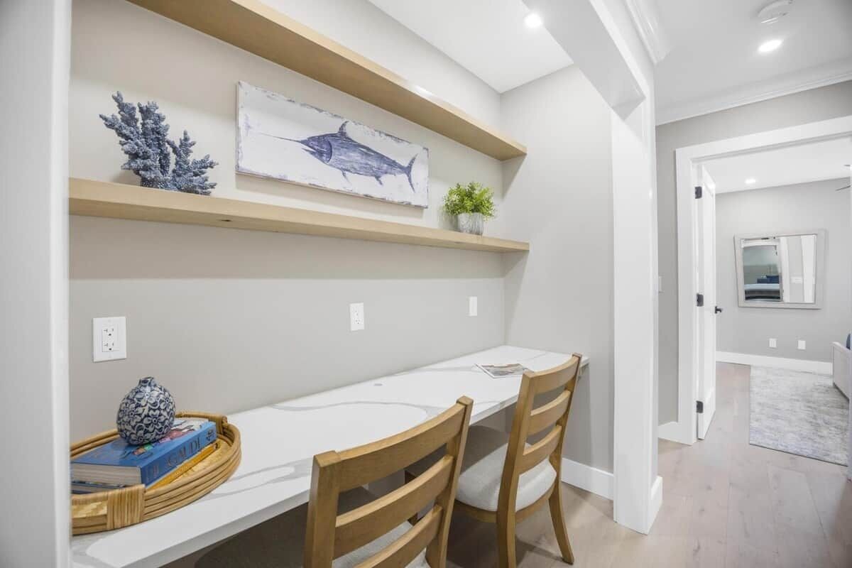 Un comedor con una mesa blanca, dos sillas de madera, un jarrón decorativo y un cuadro en la pared.