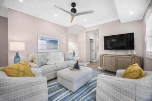 A modern living room with a sofa, ottoman, and two armchairs, a ceiling fan, a flat-screen TV, and a framed picture on the wall. - Lovely Day Chalet - Private Pool in Old Town (Key West)