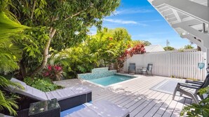 Um deck de madeira com piscina, cadeiras de descanso e vegetação exuberante.