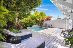 Eine Holzterrasse mit Pool, Liegestühlen und üppiger Bepflanzung.