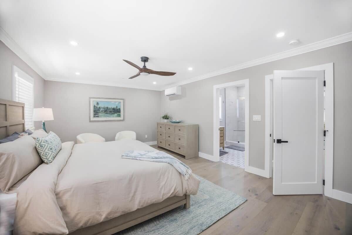 Une chambre à coucher comprenant un lit, un ventilateur de plafond, une commode et une porte donnant sur une autre pièce.