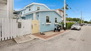 Um edifício residencial com cerca branca de piquete, portão amarelo e uma scooter estacionada.