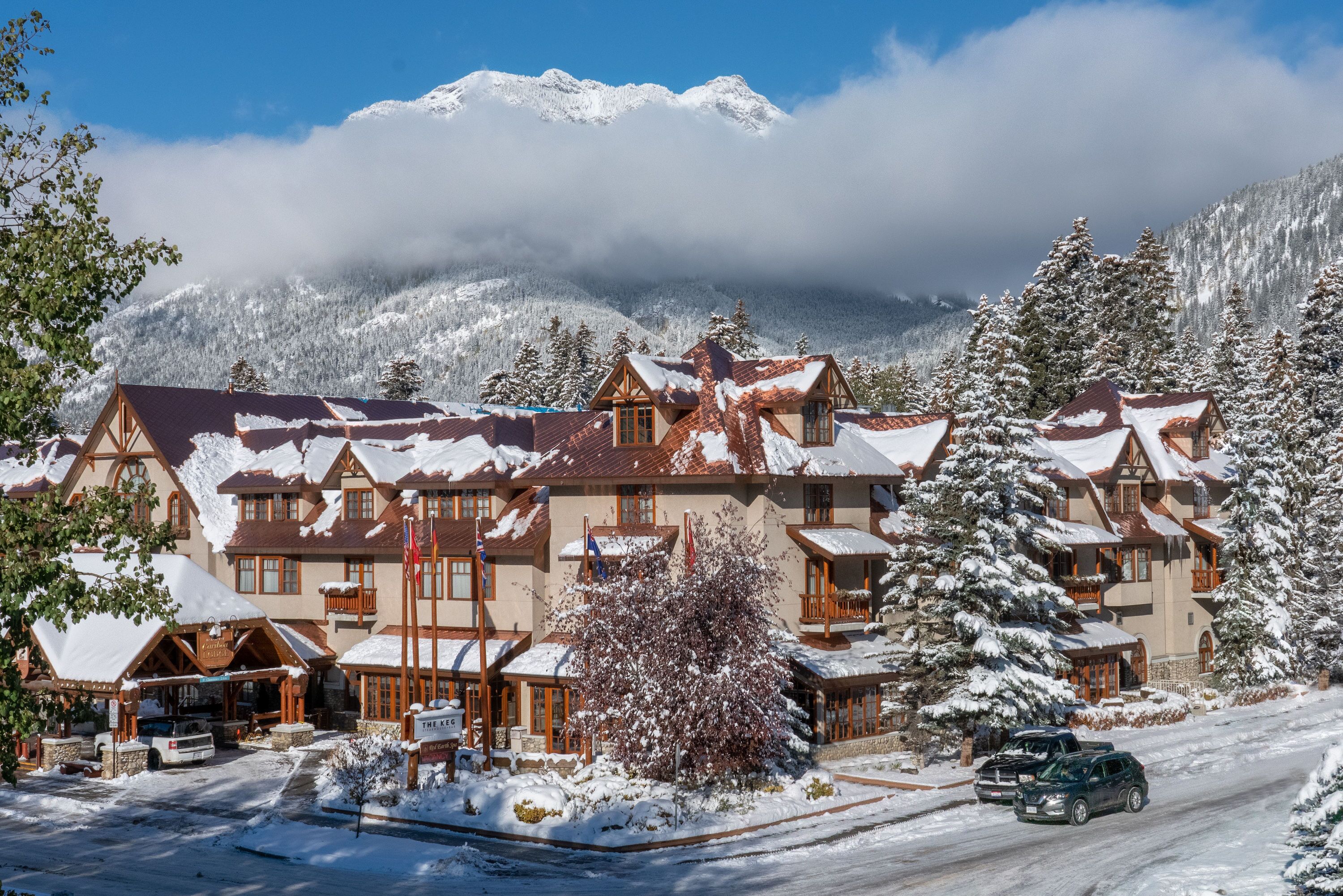 A snow-covered lodge with multiple buildings, a ski lift, and a mountain backdrop.