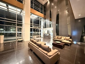 Eine großzügige Lobby mit einer großen Eckcouch, einer kleineren Sofagruppe und einem Empfangsschalter.