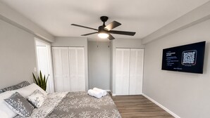 A bedroom with a bed, a ceiling fan, a TV, and a QR code on the wall.