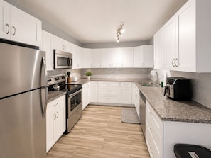 A modern kitchen with white cabinets, stainless steel appliances, and a granite countertop.