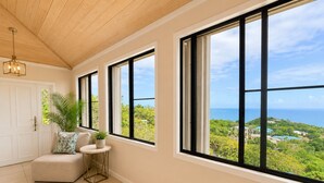 Una habitación con ventanas amplias, una puerta, una mesita, una silla y una planta.
