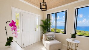 Una habitación con vista al océano, una puerta blanca, un pequeño sofá, una planta en maceta y una mesa con una lámpara.