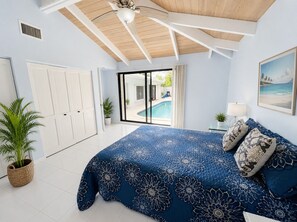 A bedroom with a large bed, a ceiling fan, a sliding glass door to a pool, and a view of the outdoors.