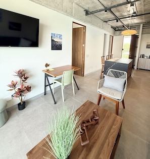 A modern living space with a dining area, a seating area with a sofa and armchairs, a coffee table, and a flat-screen TV mounted on the wall.