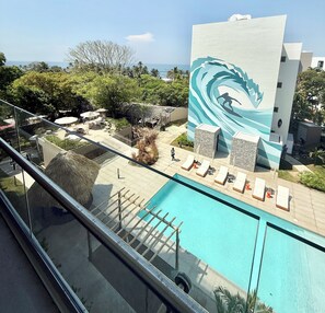 A pool area with lounge chairs, a large mural, and a view of the ocean.