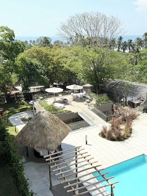 A pool area with lounge chairs, umbrellas, and a thatched-roof structure.