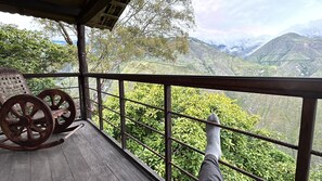 Eine Holzterrasse mit Geländer, einem Schaukelstuhl und Blick auf eine Berglandschaft.