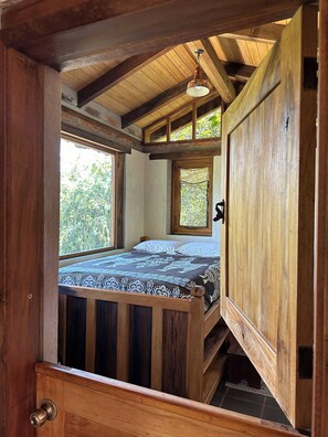 Ein Zimmer aus Holz mit einem Bett, einem Fenster und einer Tür.