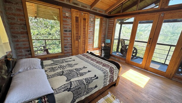 Un dormitorio con cama, piso de madera, ventanas amplias y vistas al exterior.