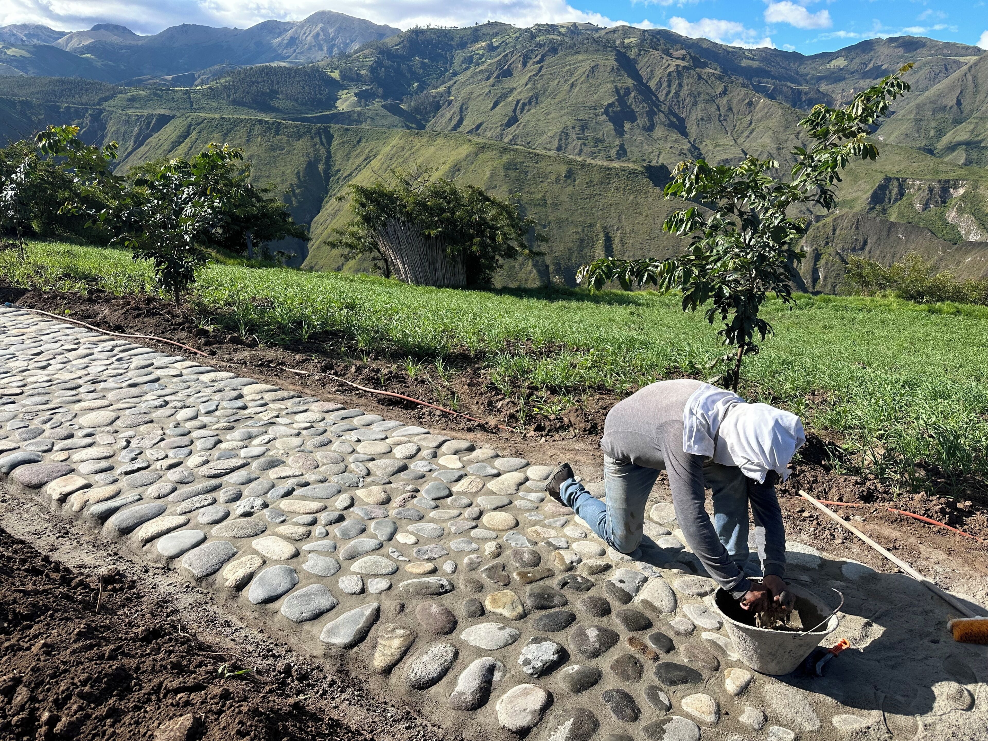 Une personne travaille sur un chemin pavé de pierres, avec un paysage montagneux en arrière-plan.