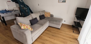 Una sala de estar con un sofá gris, una mesa de fútbol de mesa, un televisor y una escalera.