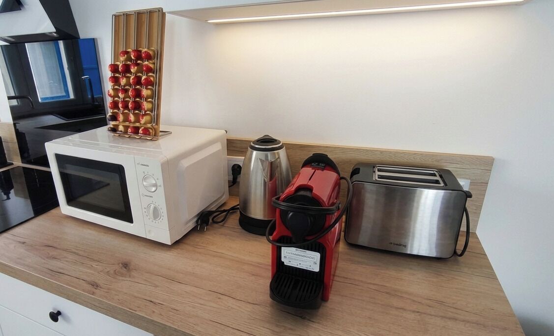 Uma cozinha equipada com micro-ondas, cafeteira, torradeira e suporte para frutas.