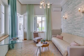 A room with a sofa, a chair, a round table, and a window with curtains. - Samouil Apartment - Near Beach  (Chania)