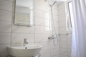 Un baño con lavamanos blanco, un espejo y una ducha.