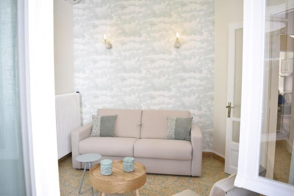A room with a beige sofa, two wall-mounted lights, a small round wooden table, and a radiator.