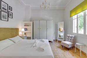 Una habitación de hotel con cama, armario, silla, una mesita y ventana.