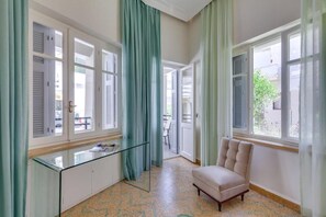 Ein Zimmer mit einem Glastisch, einem gepolsterten Sessel und großen Fenstern mit Fensterläden.