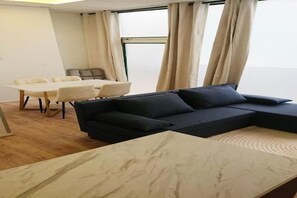 Ein modernes Wohnzimmer mit einer Eckcouch, einem Esstisch mit Stühlen und einem großen Fenster mit Vorhängen.