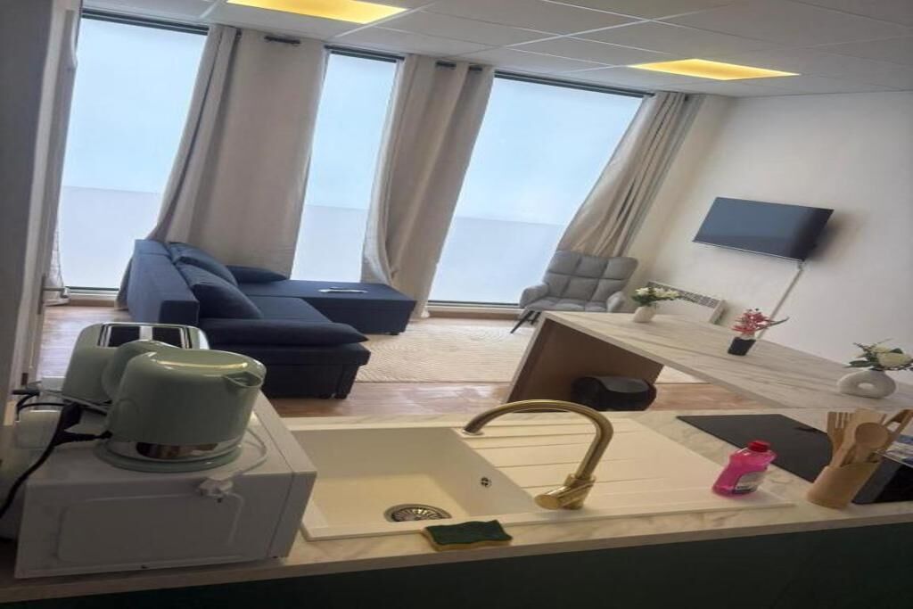 Una habitación de hotel moderna con sofá, una mesita, televisor y ventana con cortinas.