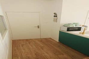 Ein Zimmer mit Holzboden, einer weißen Tür, einer türkisfarbenen Arbeitsplatte mit einer Mikrowelle und einer kleinen Pflanze.