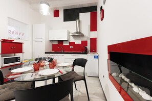 Eine moderne Küche mit Essbereich, weißen Schränken, roten Akzenten, einem Glastisch und einem integrierten Aquarium.