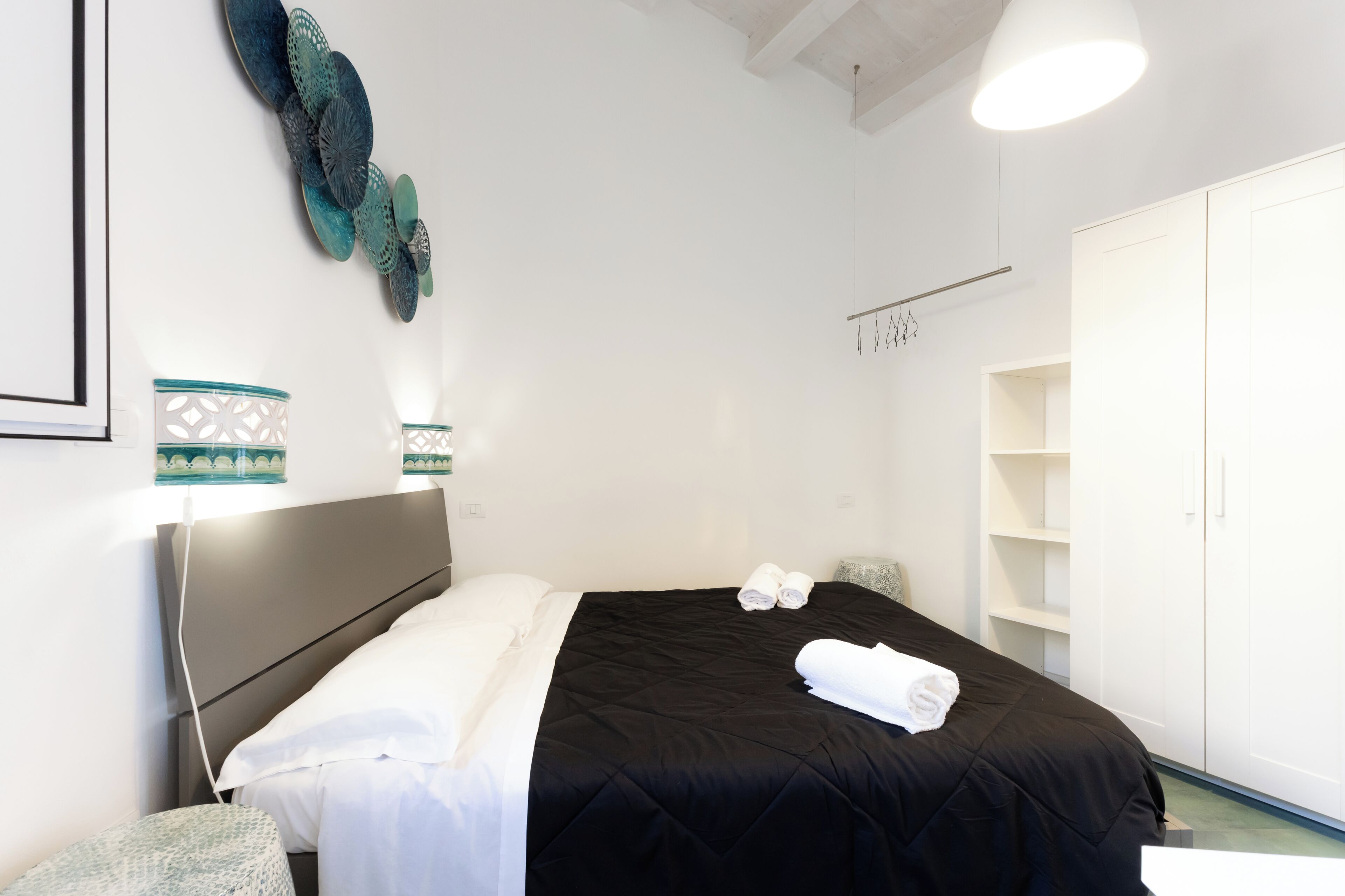 A hotel room with a bed, a wardrobe, a bedside table, and decorative wall art.