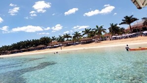 A beach with clear water, palm trees, and beach umbrellas.